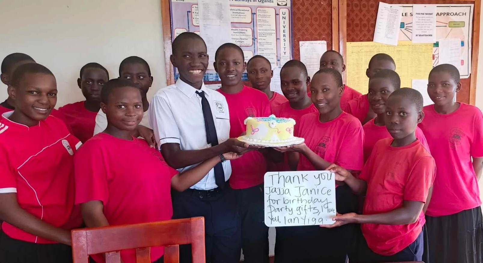 Students in red shirts holding a cake and a handwritten thank-you note